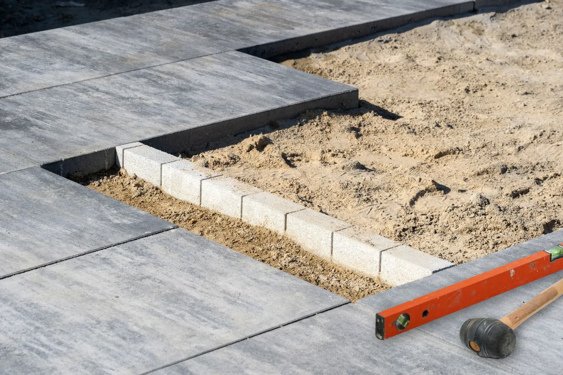 Detailaufnahme von Terrassenplatten im Verlegprozess mit Sandbett und Wasserwaage